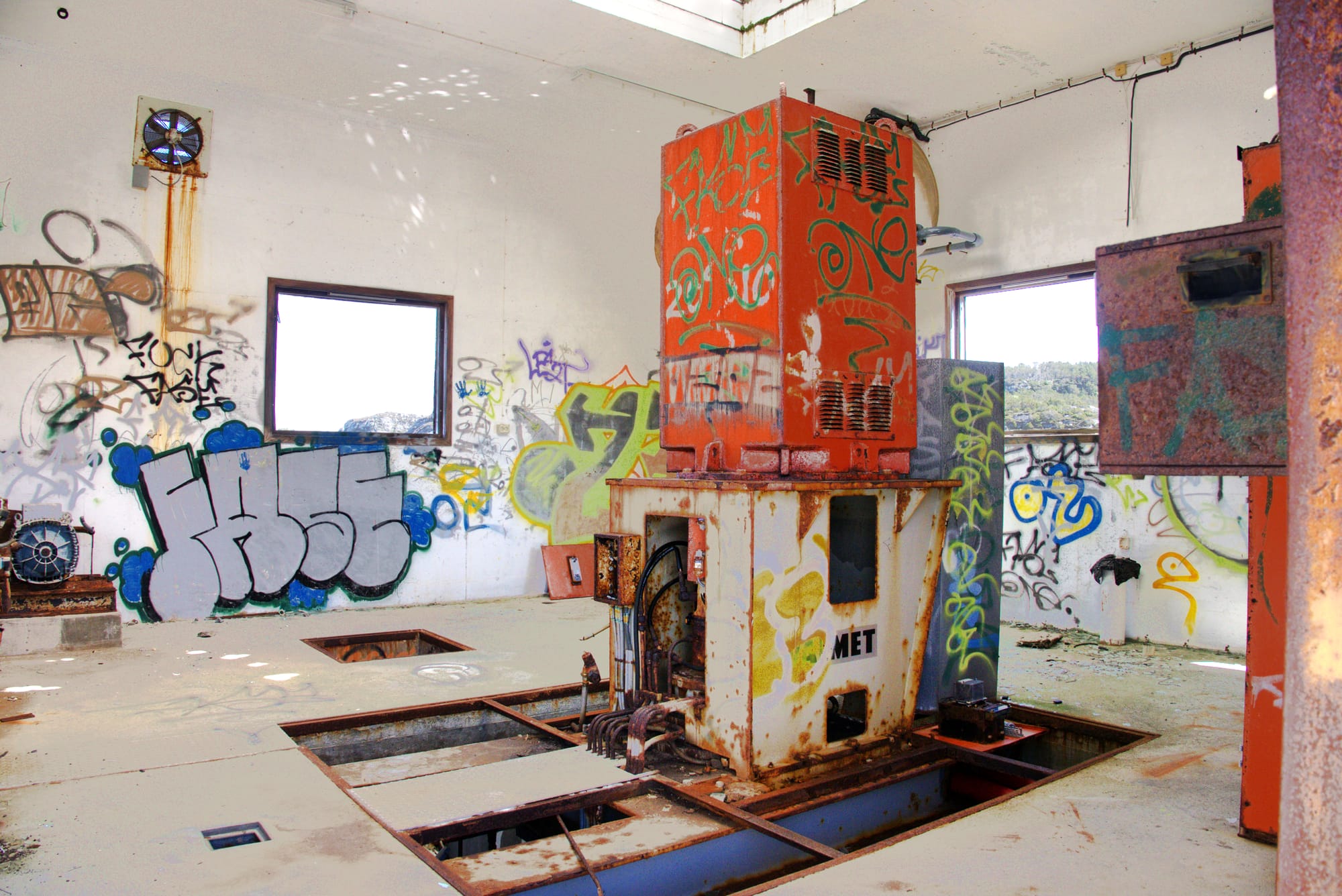 Et forfallent turbinhus med rustne maskiner og vegger dekket av fargerik graffiti. Lys strømmer inn fra vinduer og tak.